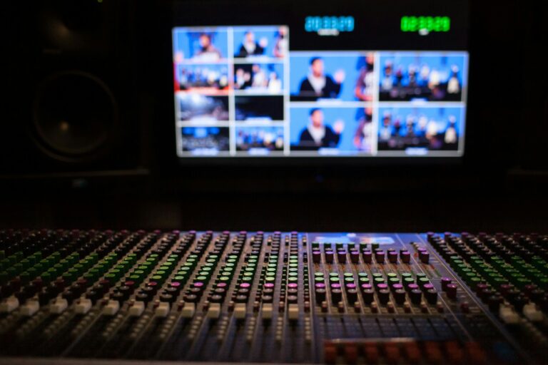 Close-up of a sound mixer with screens displaying video feeds in a professional studio setup.